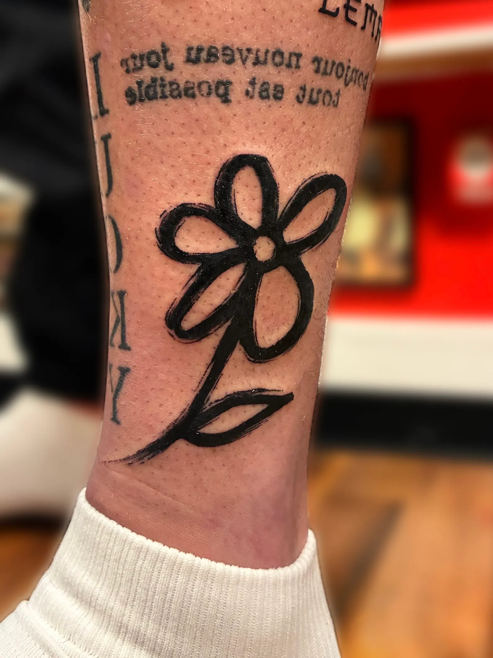 Tatouage de fleur noire au trait spontané sur la cheville