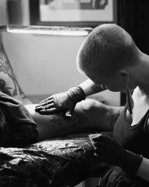 Kaiiza, concentrée, tatoue une jambe