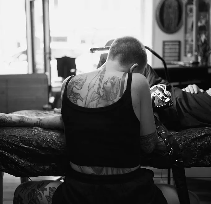 Kaiiza vue de dos pendant une séance de tatouage, dos tatoué, devant la vitrine lumineuse du studio.