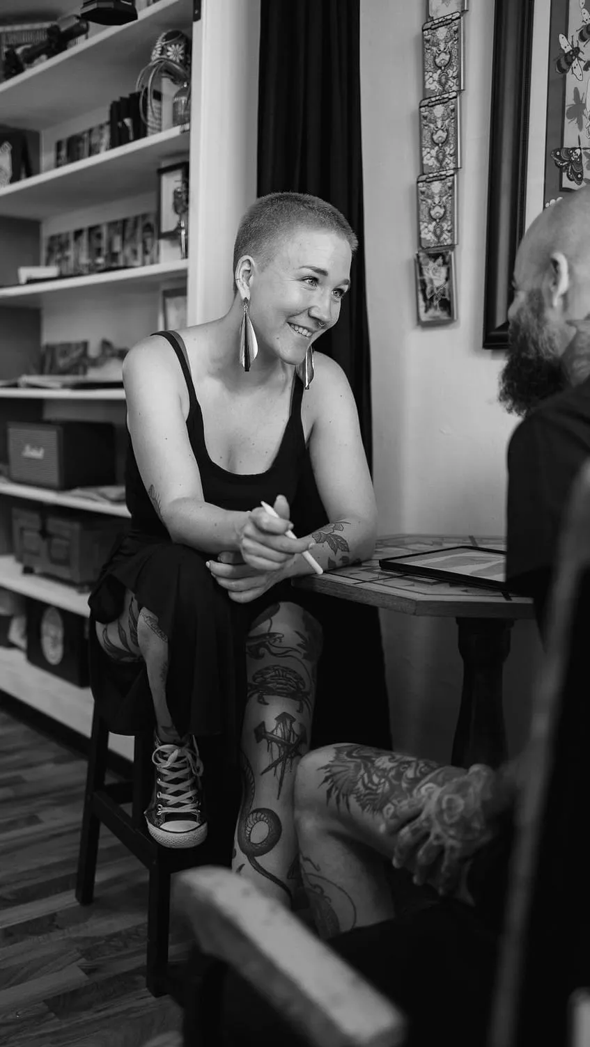 Kaiiza assise, souriante, échange avec un client au studio, bibliothèque en arrière-plan