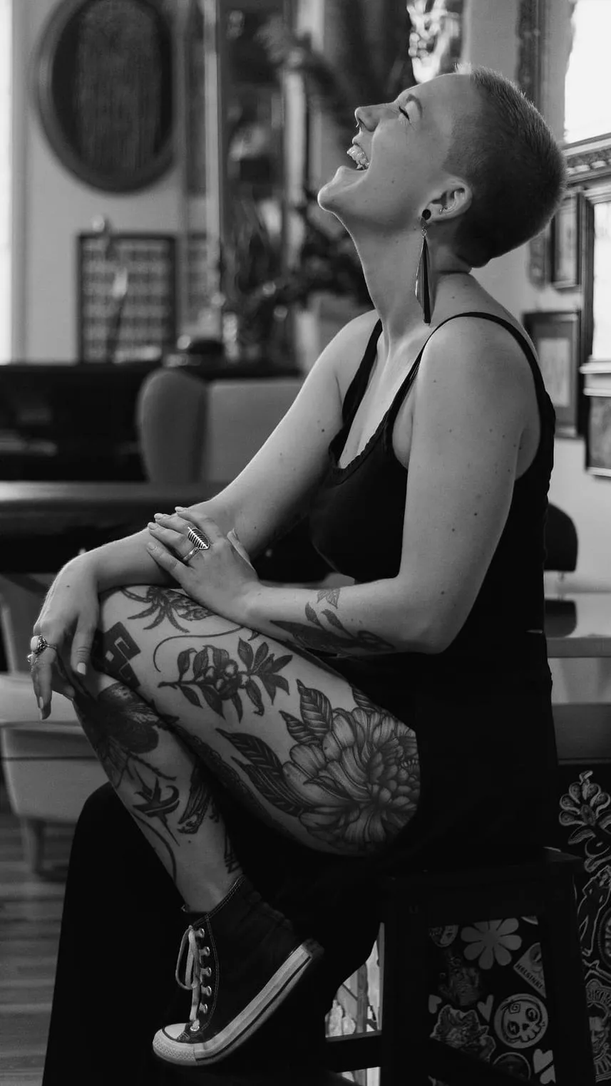 Kaiiza assise jambes croisées éclate de rire, tête levée, au milieu du studio décoré.
