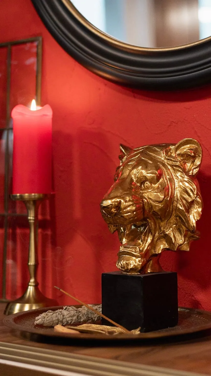 Détail de la décoration du studio : bougie rouge allumée et tête de tigre dorée devant le mur rouge.