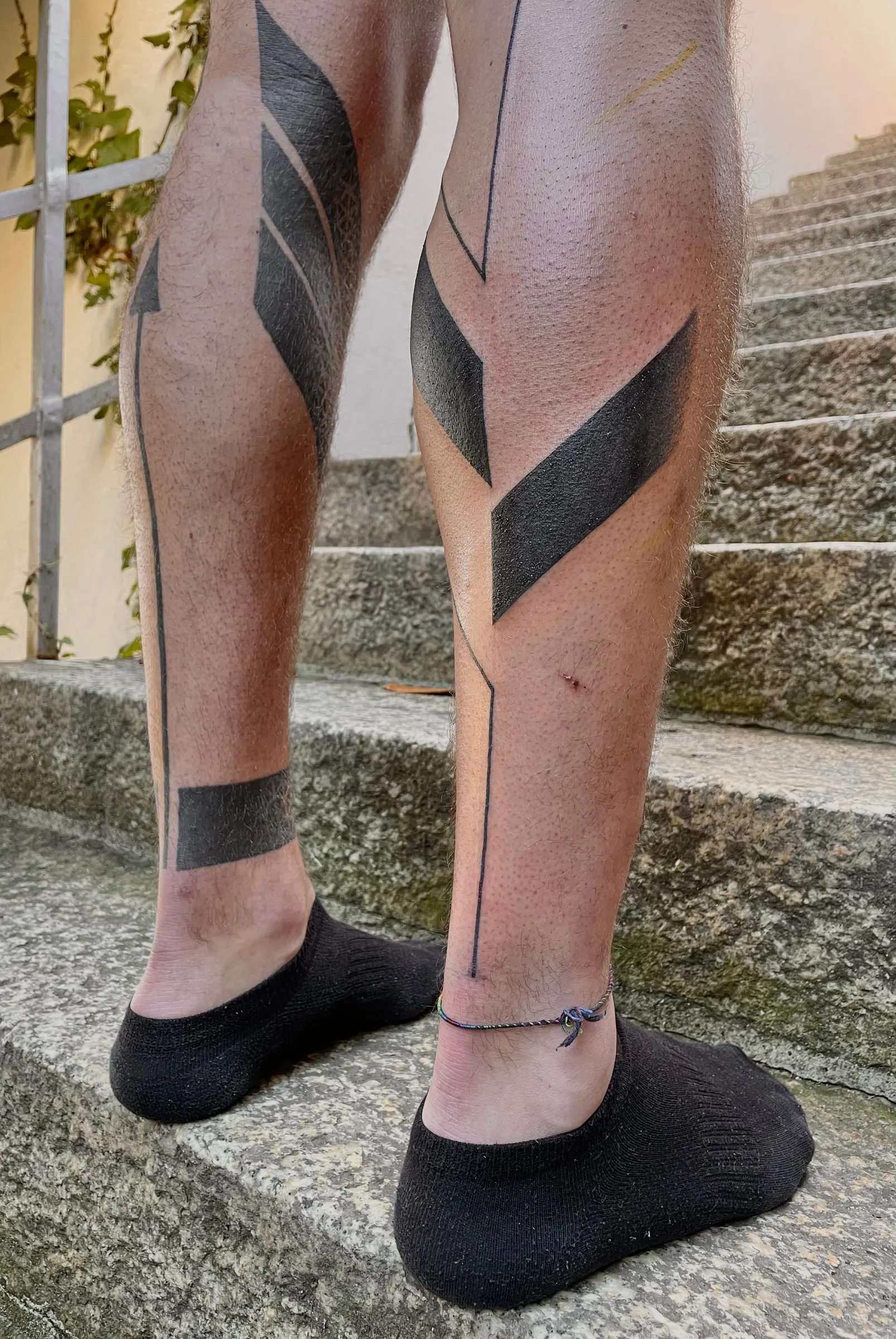 Tatouage blackwork de larges formes noires géométriques en chevrons couvrant les mollets et les chevilles
