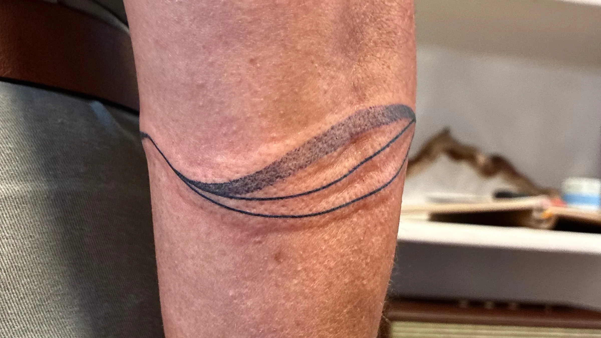 Tatouage d'un bracelet à deux lignes fines encadrant une vague ombrée, autour de l'avant-bras