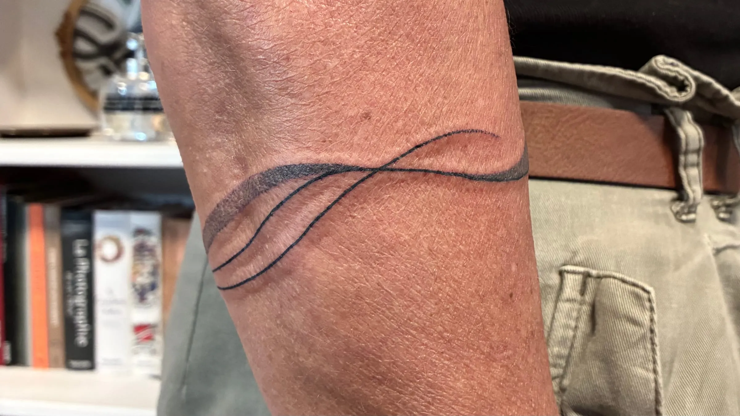 Tatouage minimaliste d'un bracelet en ligne fine formant une legere vague autour de l'avant-bras