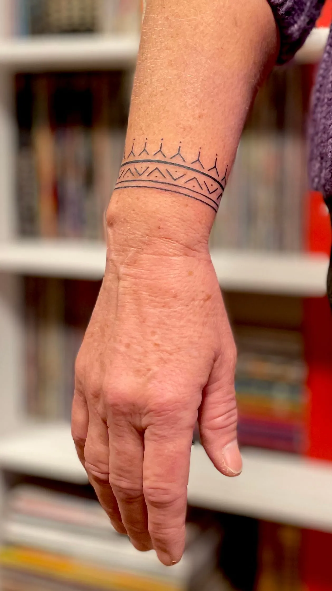 Tatouage fineline d'un bracelet ornemental a motifs geometriques, triangles et petites pointes, autour du poignet.