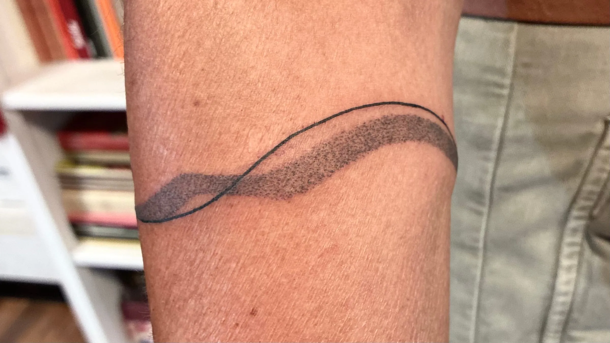 Tatouage d'un bracelet composé d'une ligne fine et d'une vague ombrée en pointillisme, autour du bras