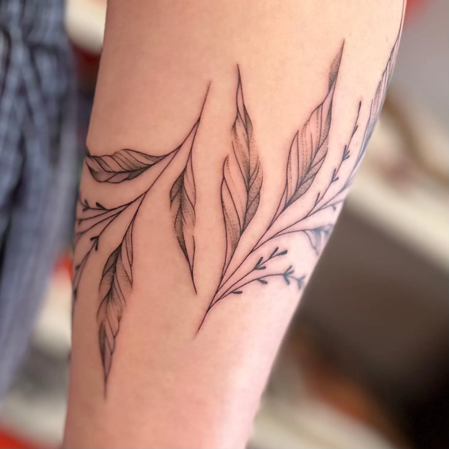 Tatouage fineline en gros plan de feuilles allongées ombrées de pointillés, sur l'avant-bras