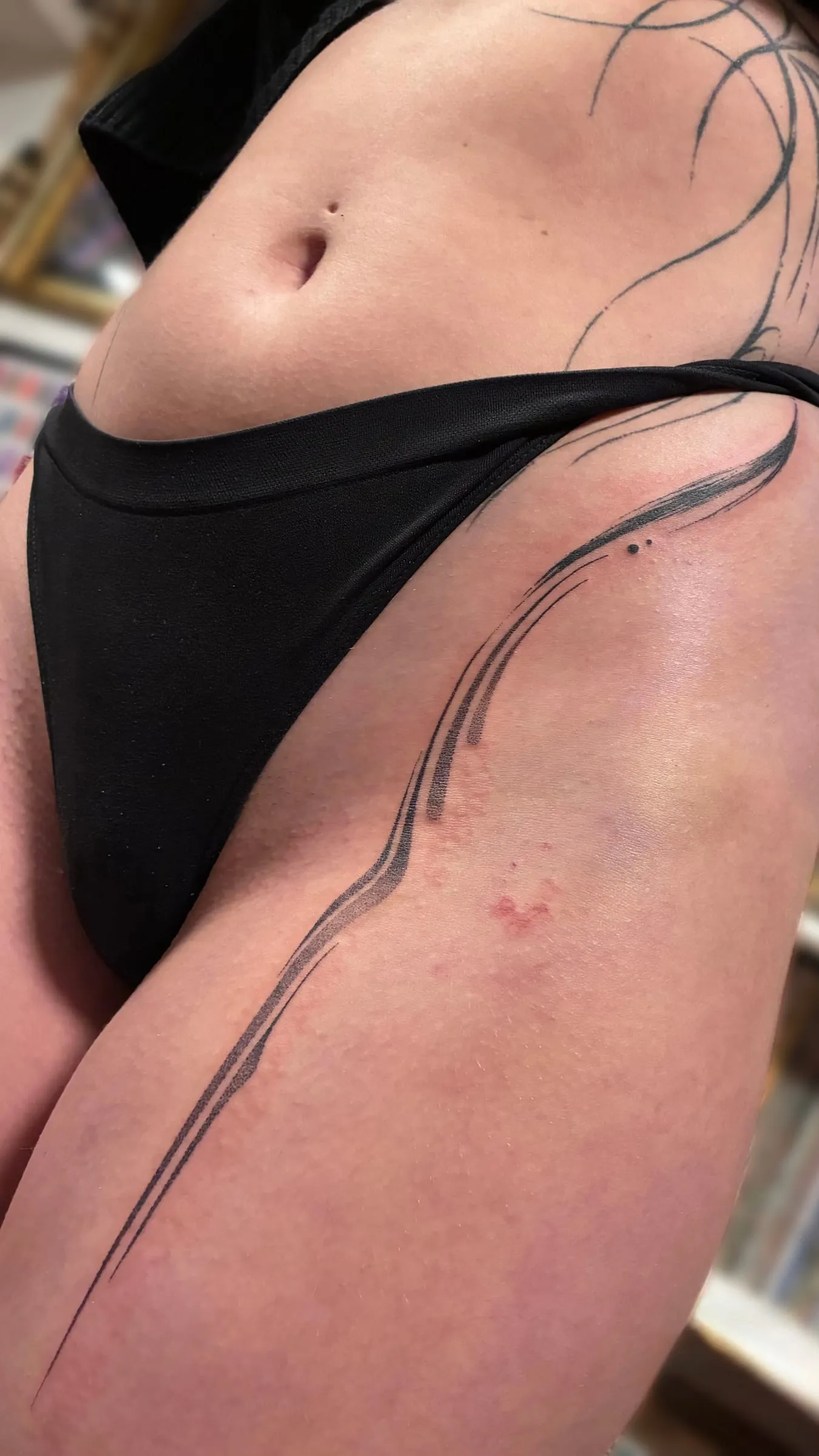 Tatouage abstrait d'une fine ligne courbe qui descend le long de la hanche