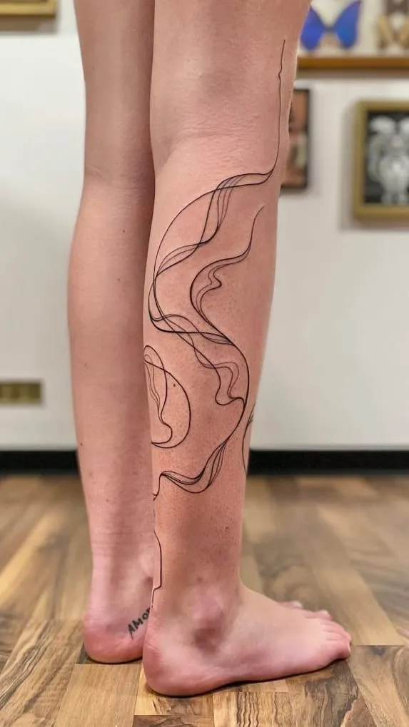 Tatouage fineline aux lignes abstraites qui s'étirent sur le côté de la jambe, encre noire