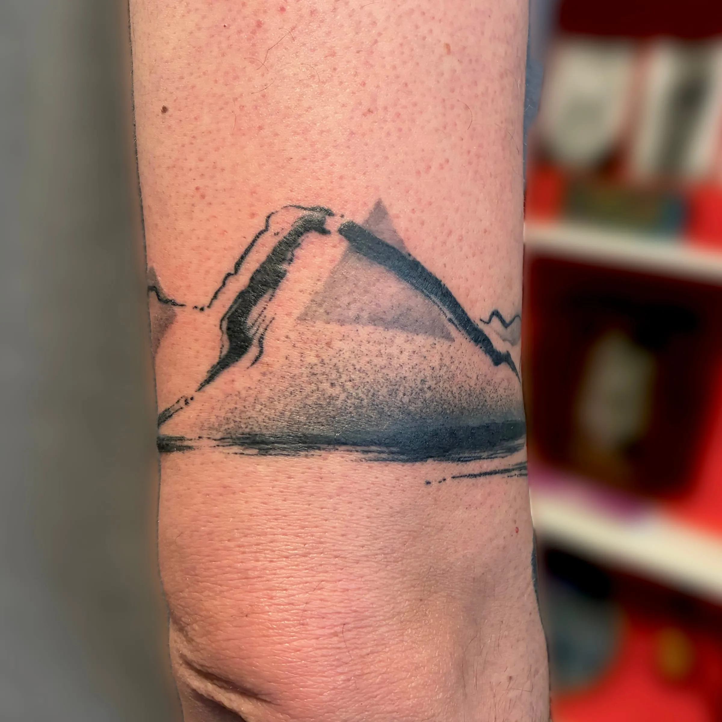 Tatouage abstrait d'une montagne triangulaire réalisée au trait de pinceau et en pointillés, avec son reflet, sur le bras