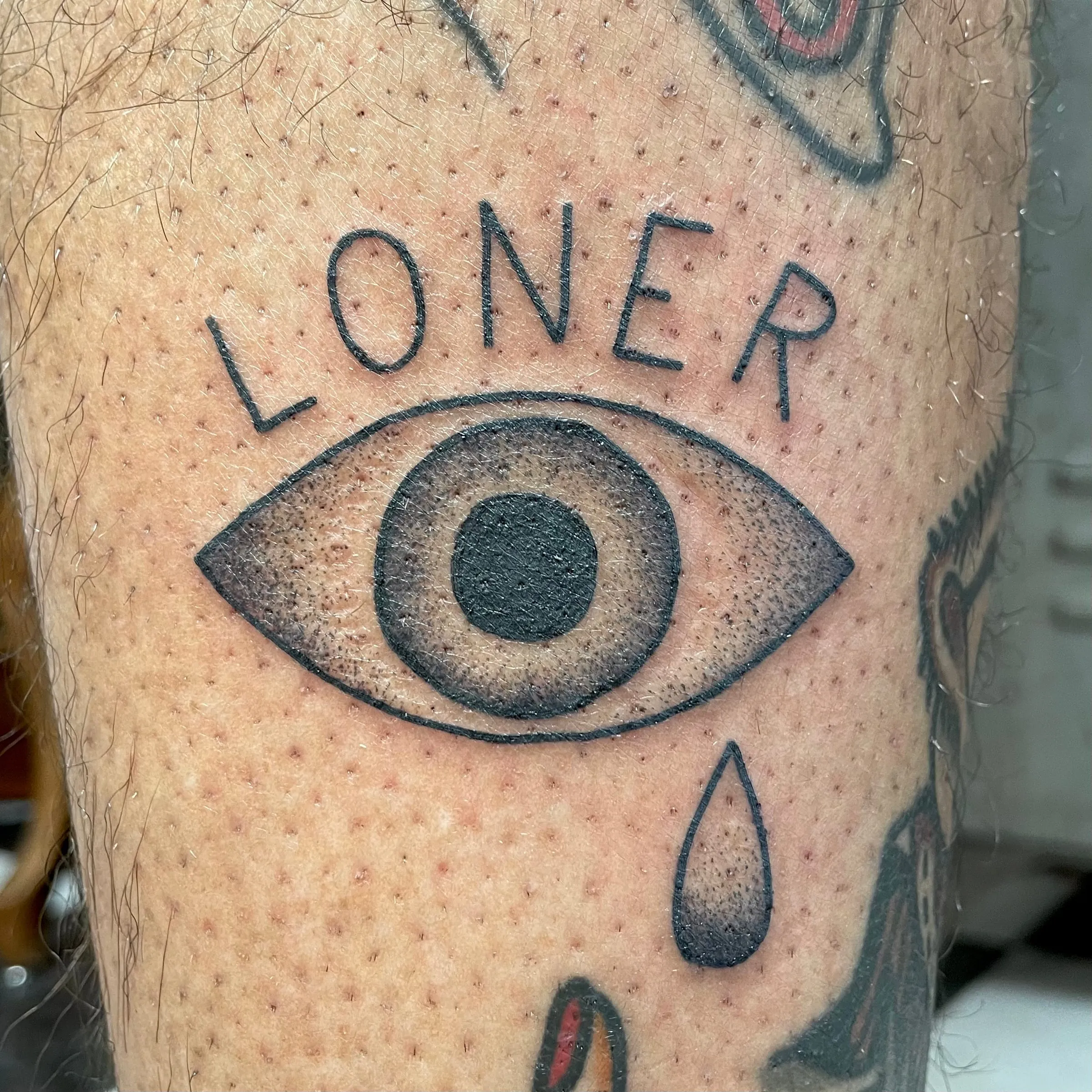 Tatouage d'un oeil traditionnel surmonte du mot Loner avec une larme, style old school