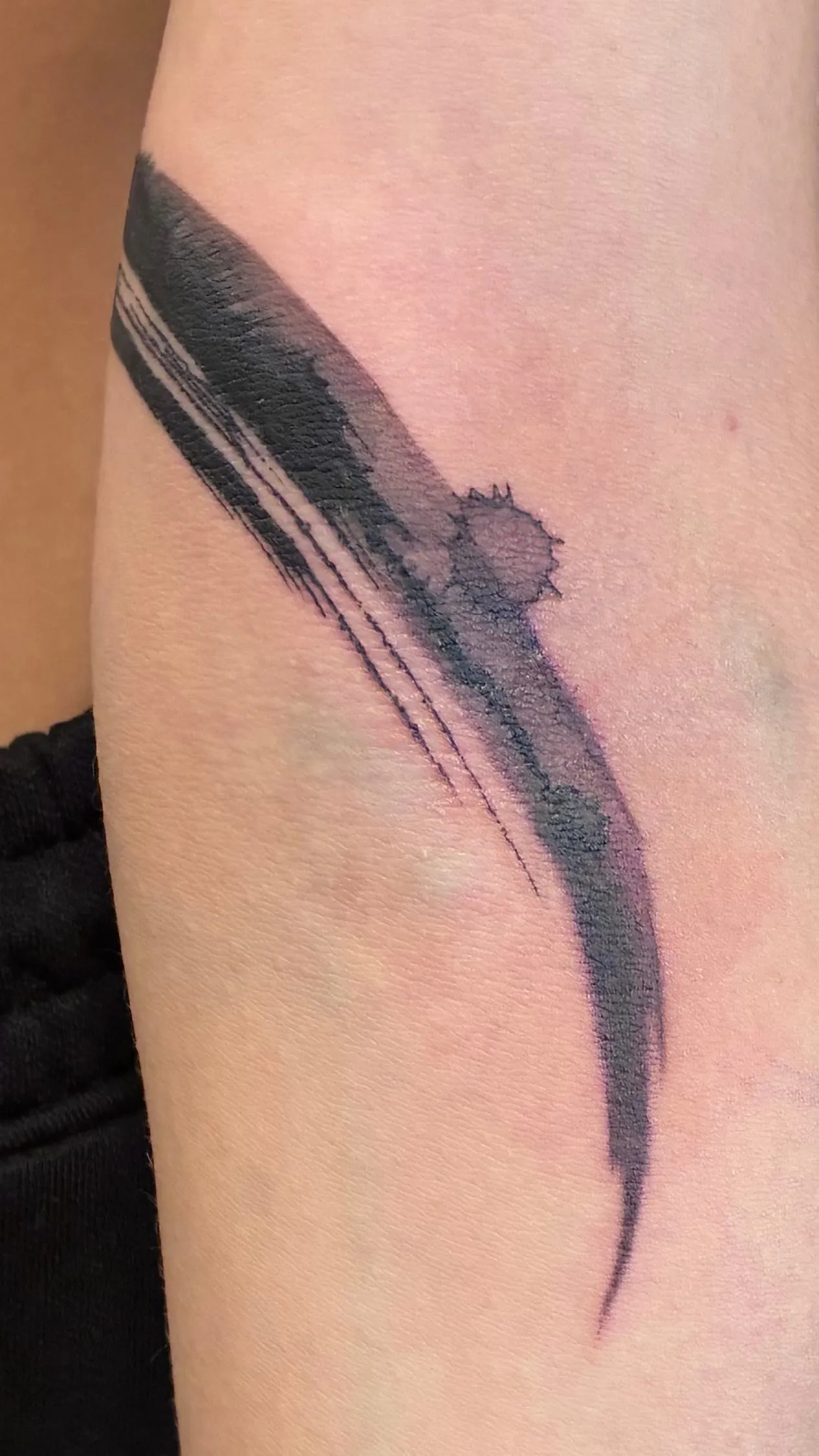Tatouage abstrait en coup de pinceau noir ponctué d'une projection d'encre, sur le bras