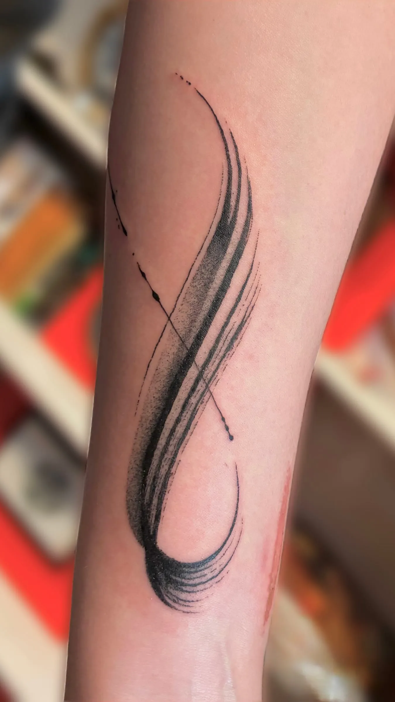 Tatouage abstrait d'un trait de pinceau noir formant une boucle fluide sur l'avant-bras