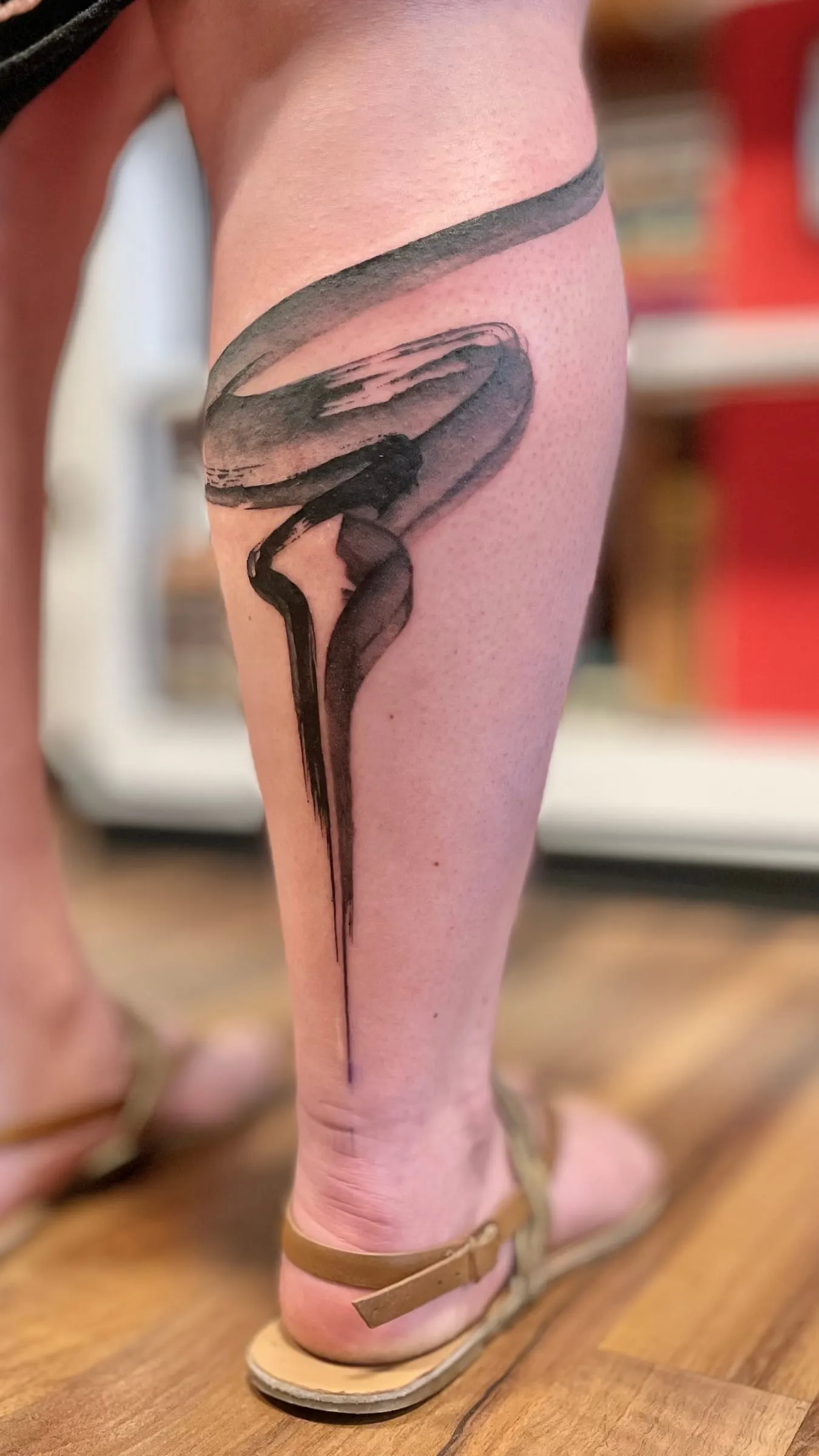 Tatouage abstrait en coups de pinceau noirs et gris qui s'enroulent autour du mollet, style peinture.