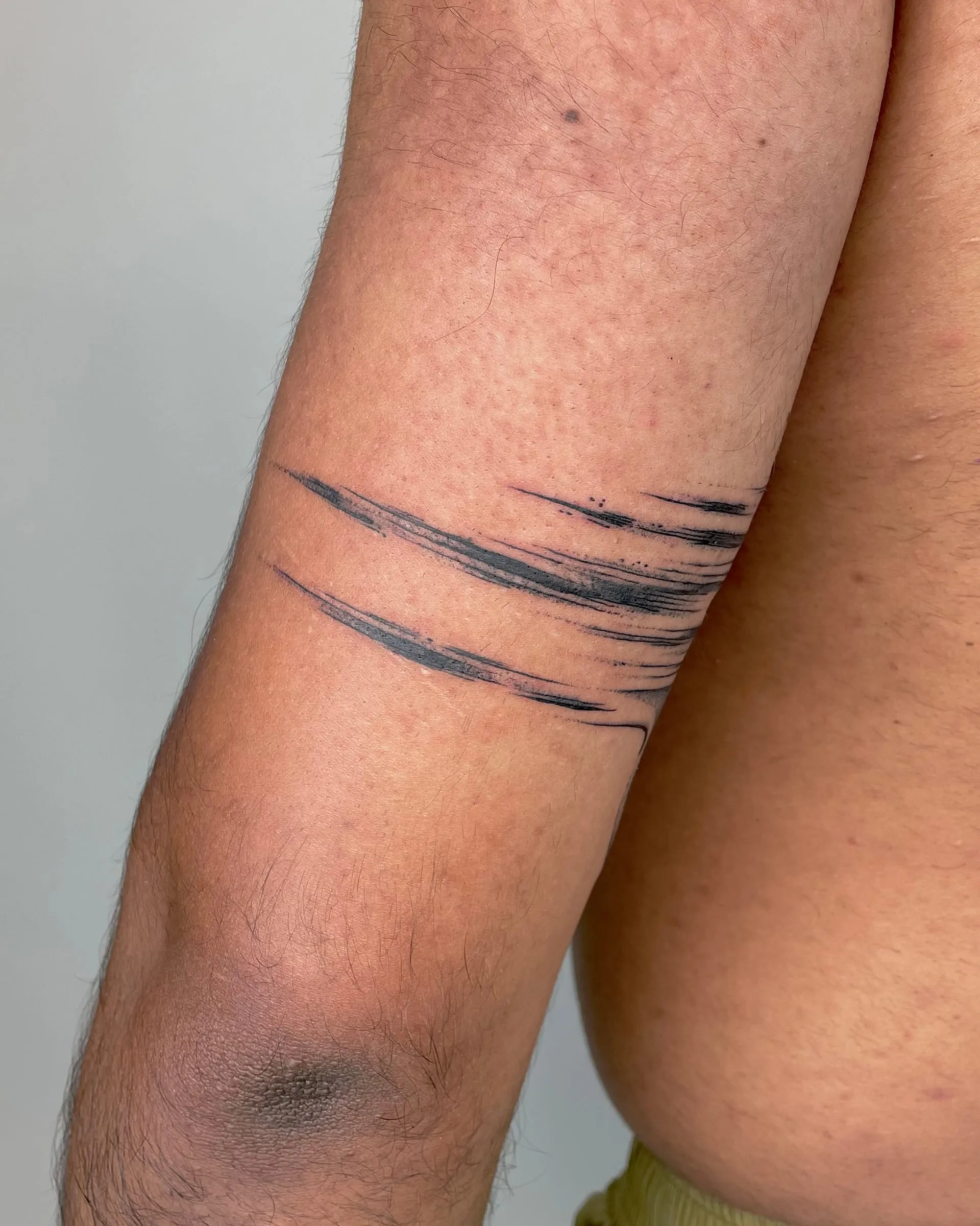 Tatouage de traits de pinceau noirs formant un bracelet abstrait autour du bras