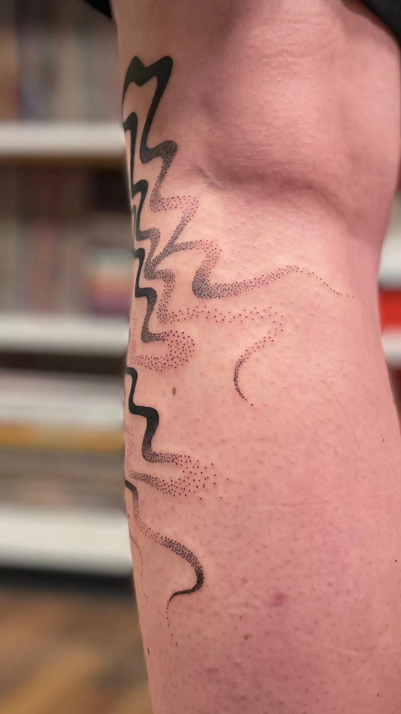 Tatouage abstrait d'une ligne noire ondulee prolongee par un nuage de points en degrade, sur le bras.