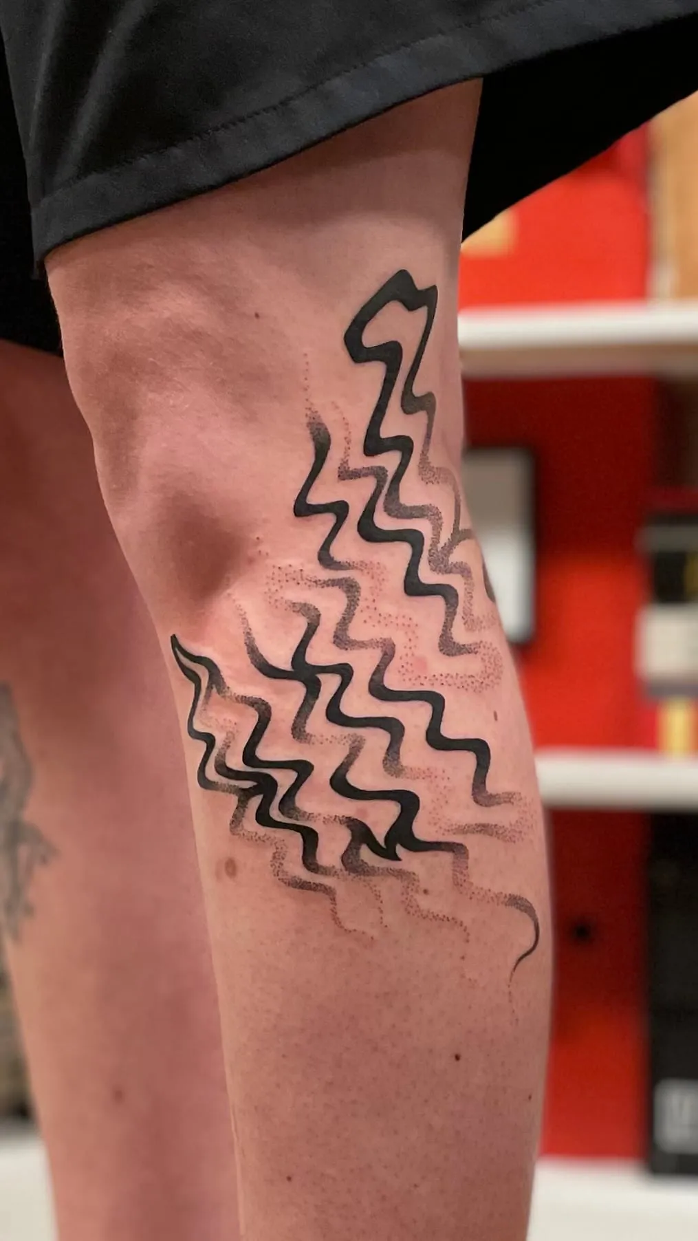 Tatouage abstrait d'un ensemble de lignes noires ondulées en zigzag couvrant le genou et le mollet.