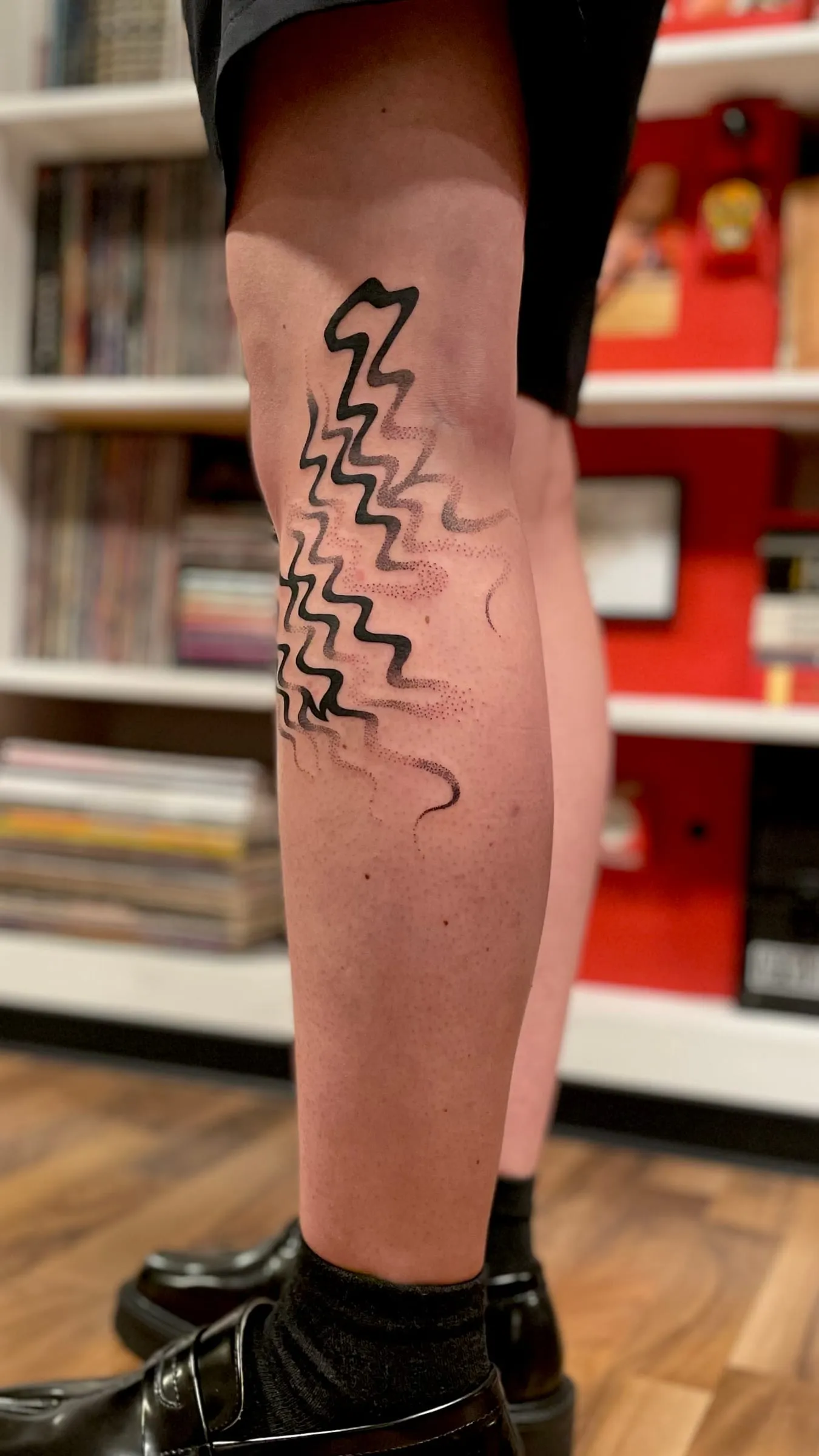 Tatouage abstrait de lignes noires ondulees en zigzag descendant le long de la jambe.